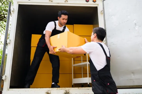 Dos trabajadores de mudanzas foráneas cargando cajas de cartón dentro de un camión.