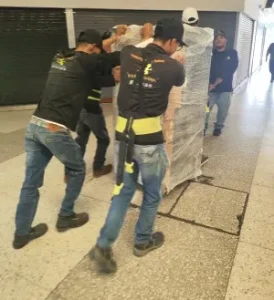 Equipo de trabajadores moviendo carga pesada embalada usando arnés de seguridad en pasillo para mudanzas compartidas.