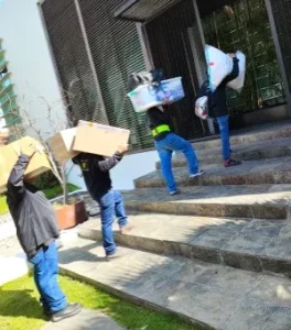 Personal subiendo cajas y contenedores por escaleras de piedra en un servicio residencial de mudanzas compartidas.