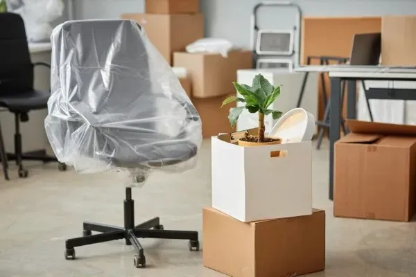 Silla giratoria protegida con plástico y cajas apiladas listas para el transporte en una mudanza de oficina.